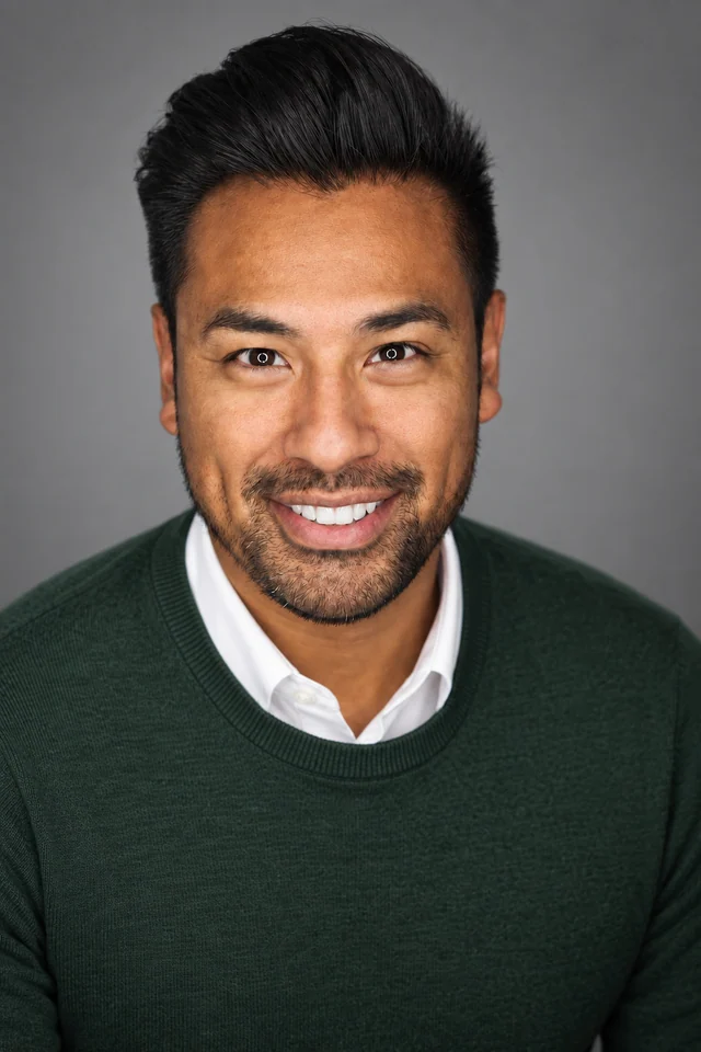 Professional headshot of the same man wearing a forest-green sweater over a white shirt.