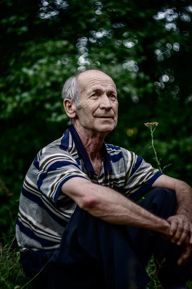 Original outdoor photo of an older man with gray hair and visible facial lines wearing a striped polo shirt.